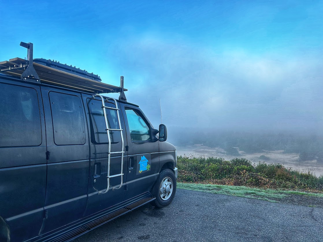 black camper van parked on a hill with a view of sand dunes below