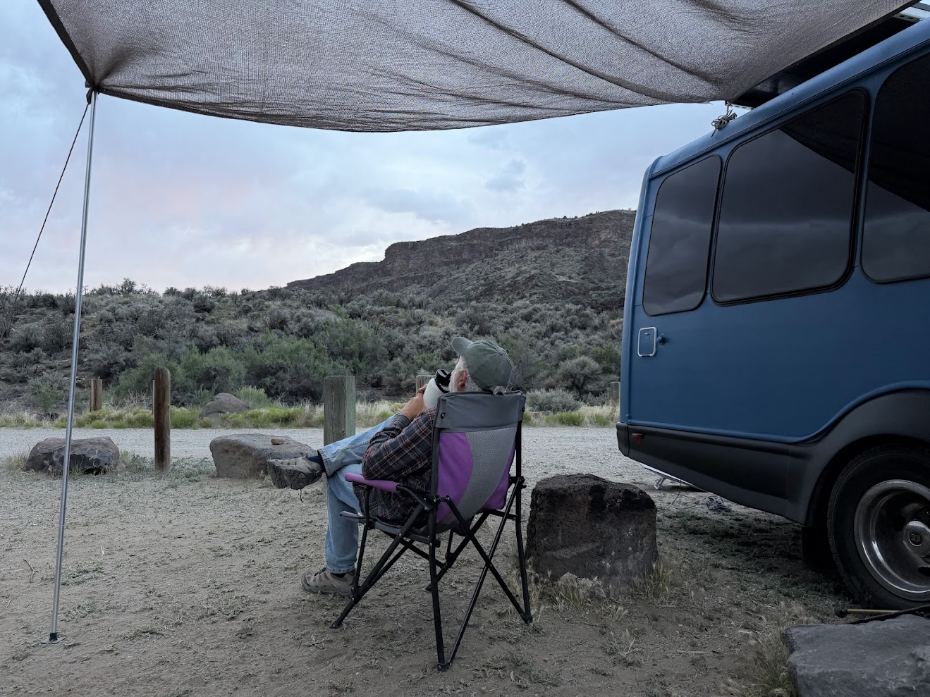 man sitting in a camp chair beside a blue bus